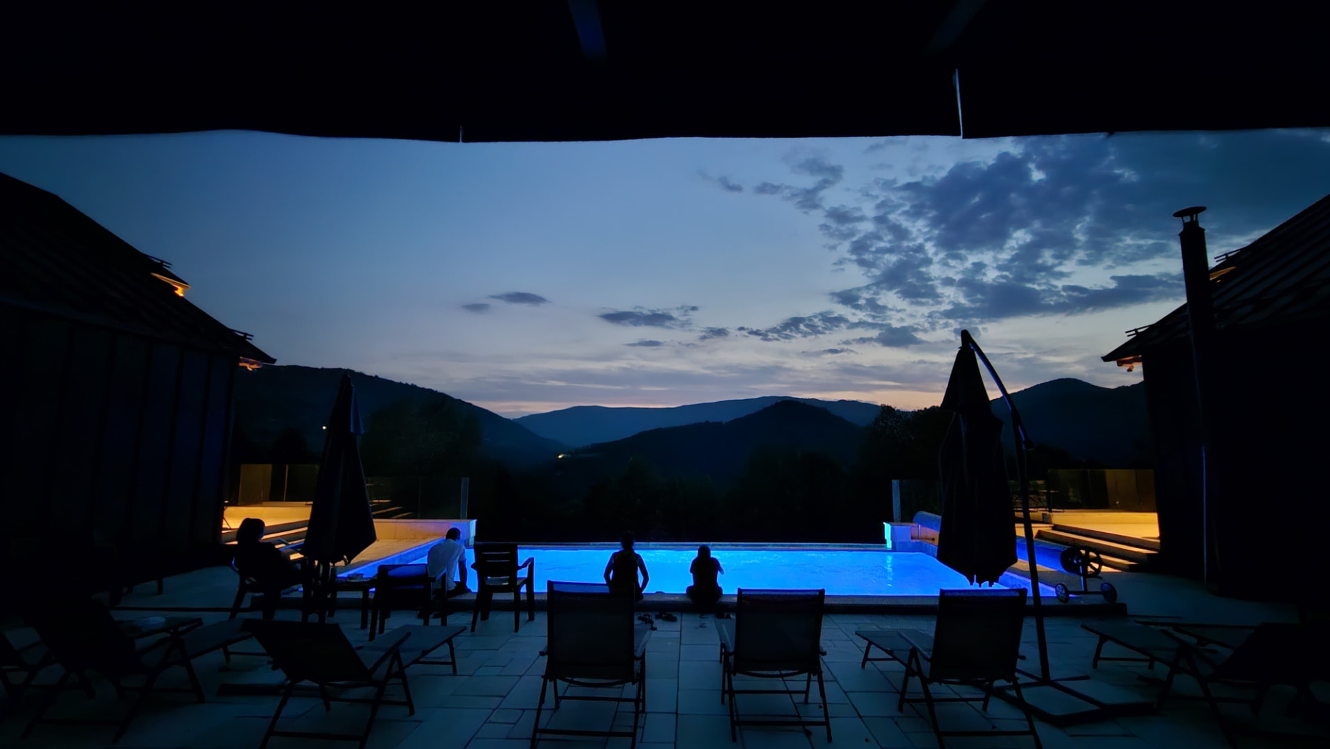 Guests by the lit pool, taking in the mountain ridges in the last light of evening