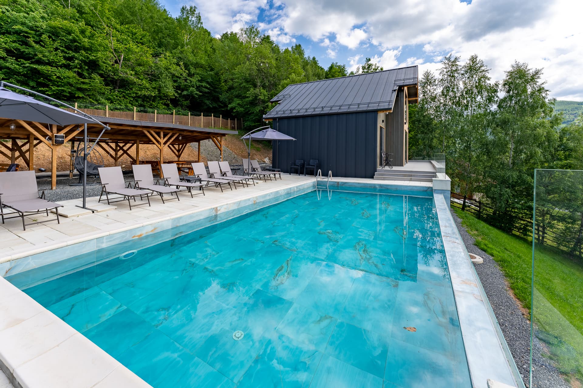 Outdoor area at Cabanele Carmel: the pool, sun loungers and the wooden gazebo by the forest