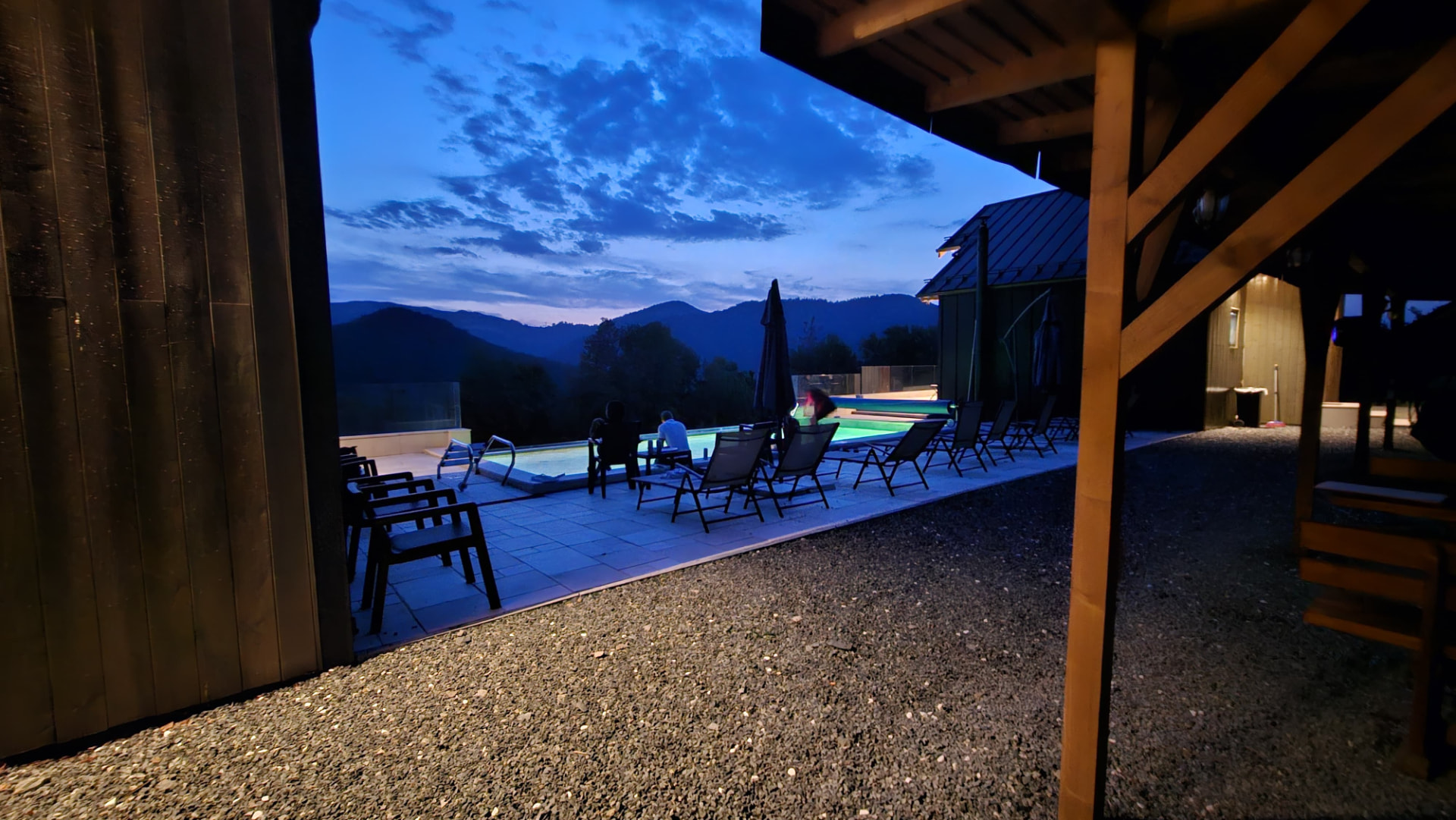Guests seated by the pool in the evening, seen from beneath the wooden eaves