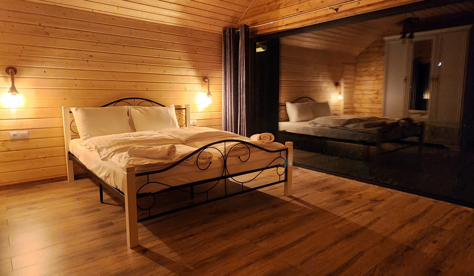 A bedroom with timber-clad walls, a double bed and warm light from the wall sconces