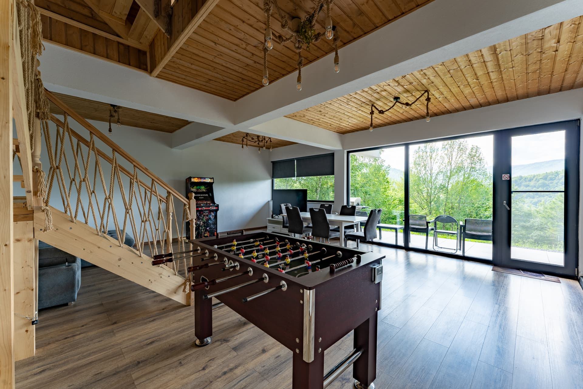 Living area of a Carmel cabin, with a foosball table, wooden staircase and large windows facing the terrace
