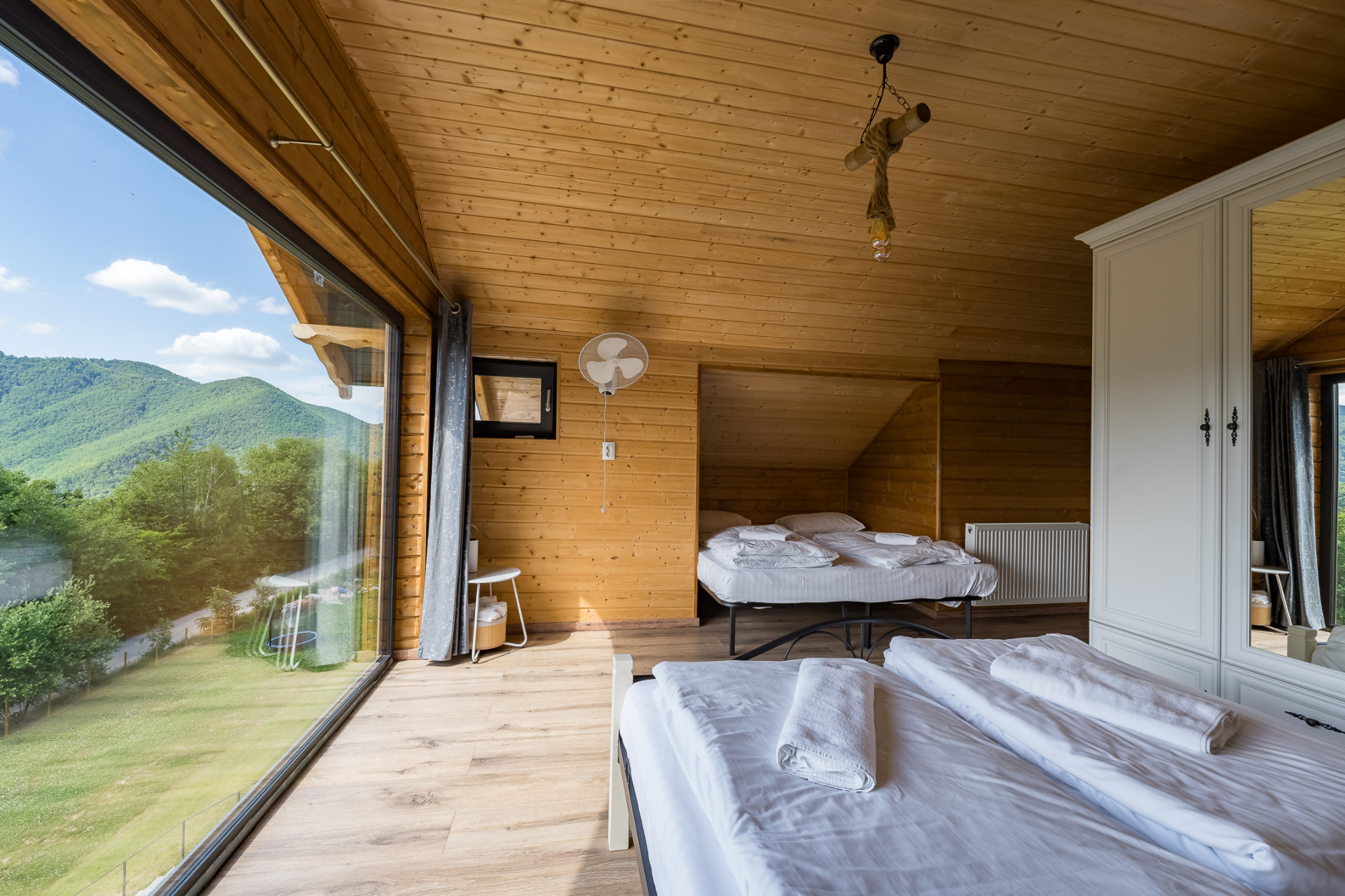 Interior of a bedroom at Cabanele Carmel, with wooden walls, two beds and a panoramic window facing the mountain
