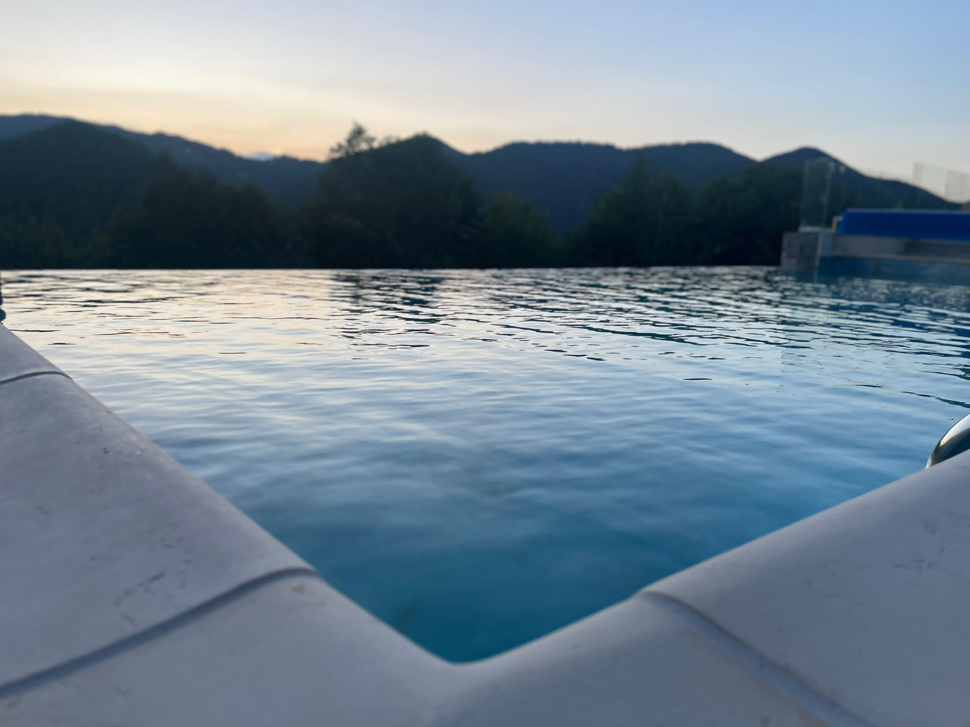 The pool's edge at water level, with the mountains in the soft evening light