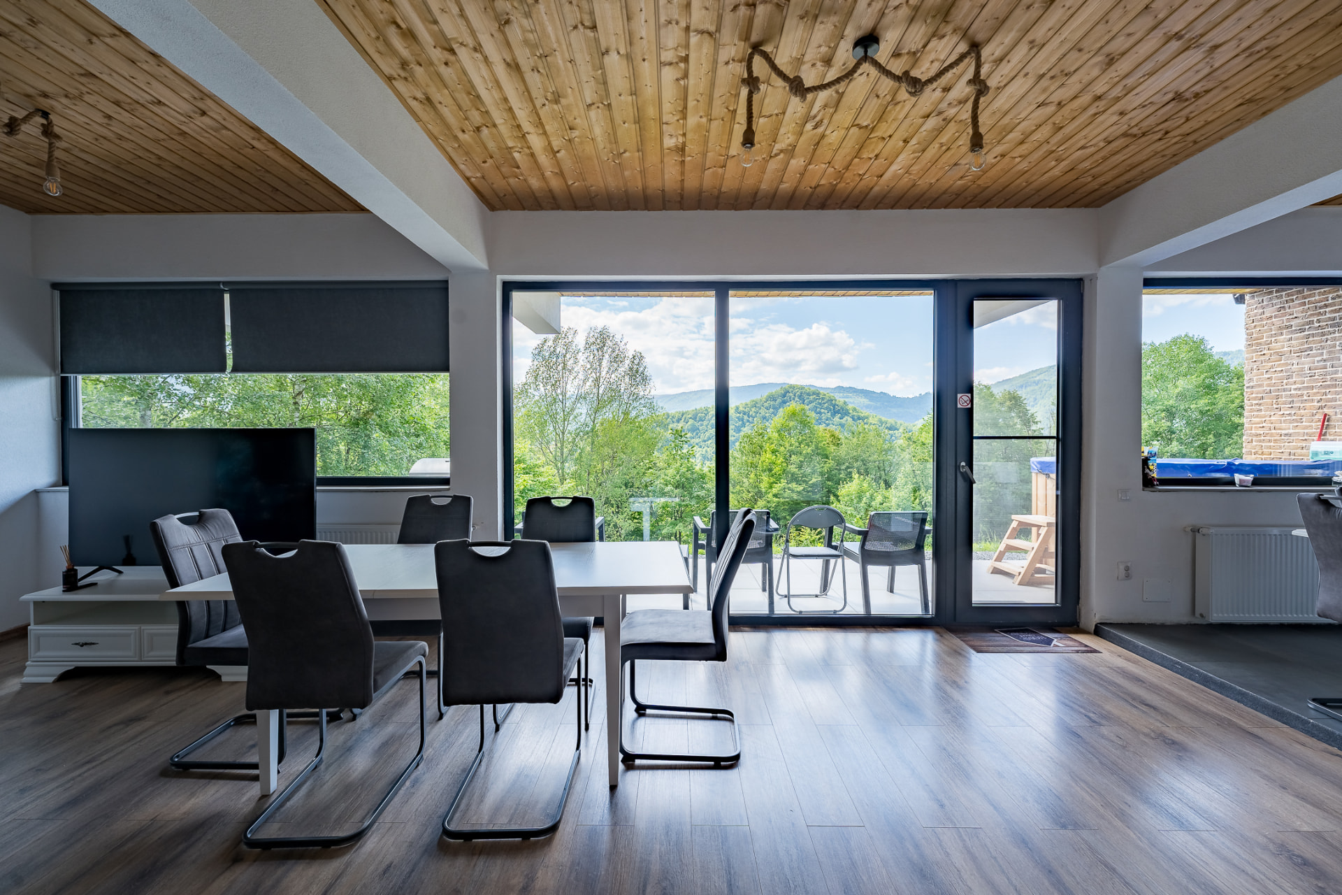 A living room with a long dining table and panoramic windows opening onto the terrace and surrounding hills