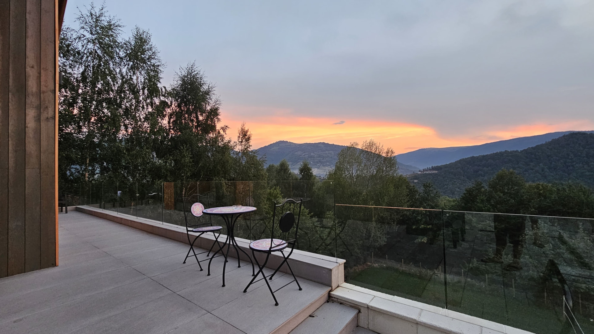 The terrace at Cabanele Carmel at sunset — two chairs and a small table, with the mountains and valley in the evening light