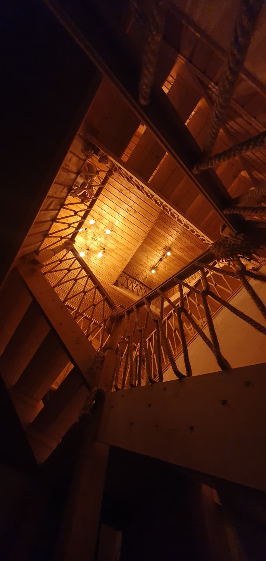 An interior architectural detail: the tall wooden ceiling and rope railing, at dusk