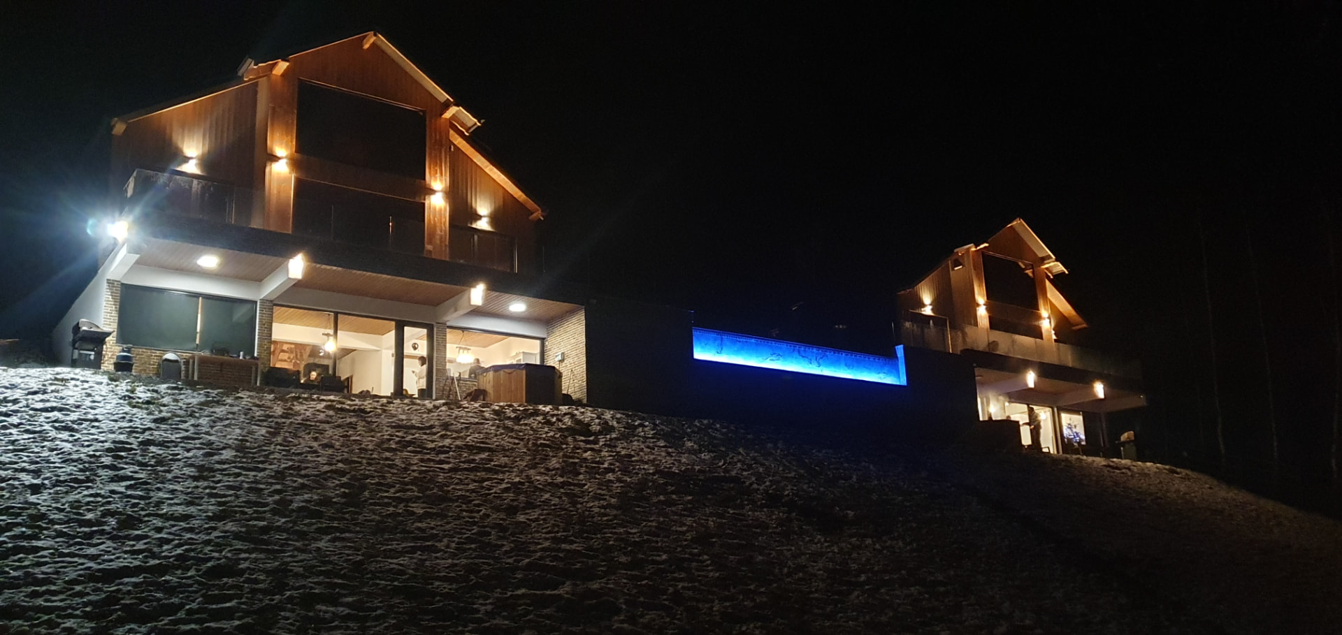 The two cabins lit up on a winter night, with the blue-lit pool between them