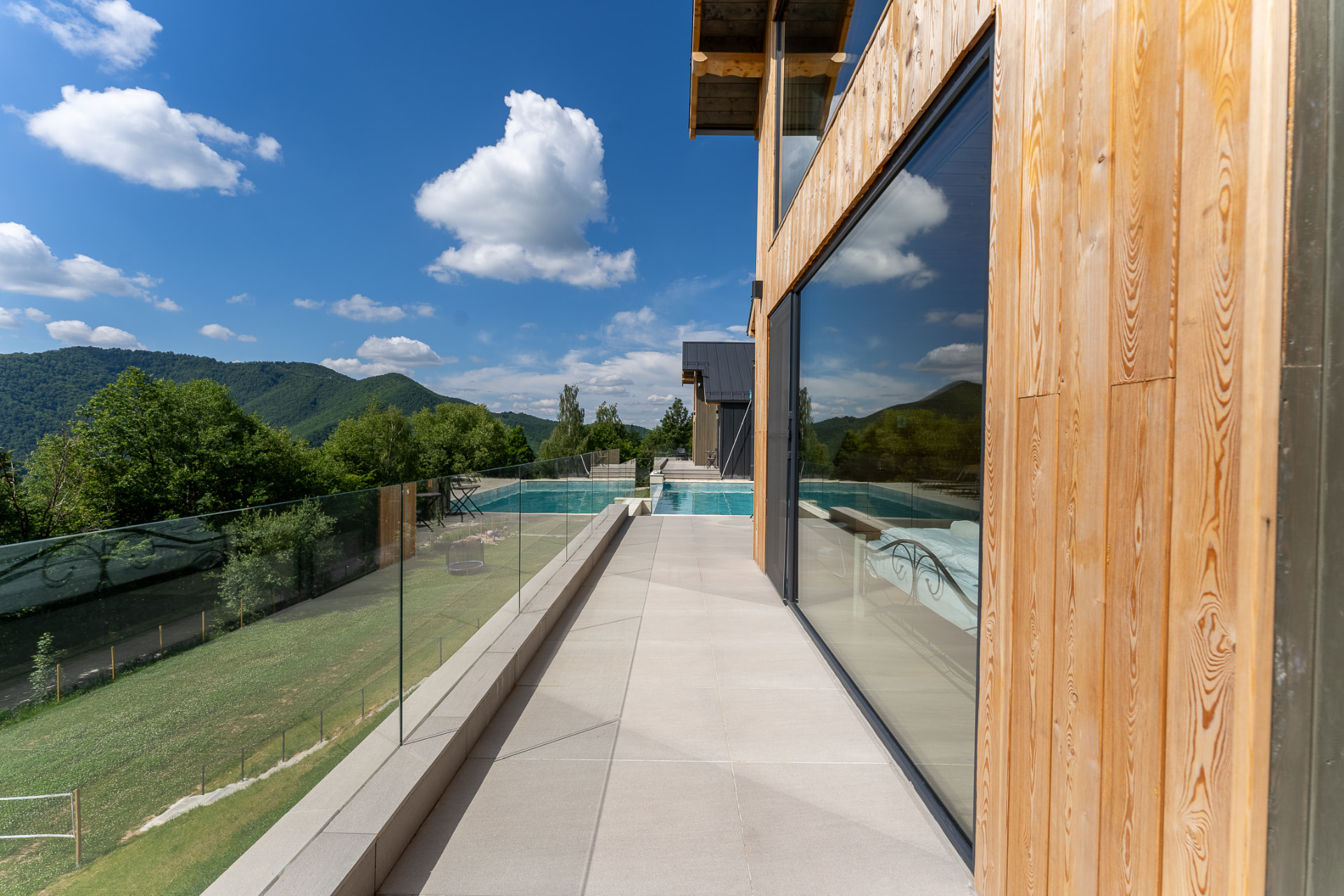 The narrow terrace beside the timber façade, with a glass railing and the pool in the distance