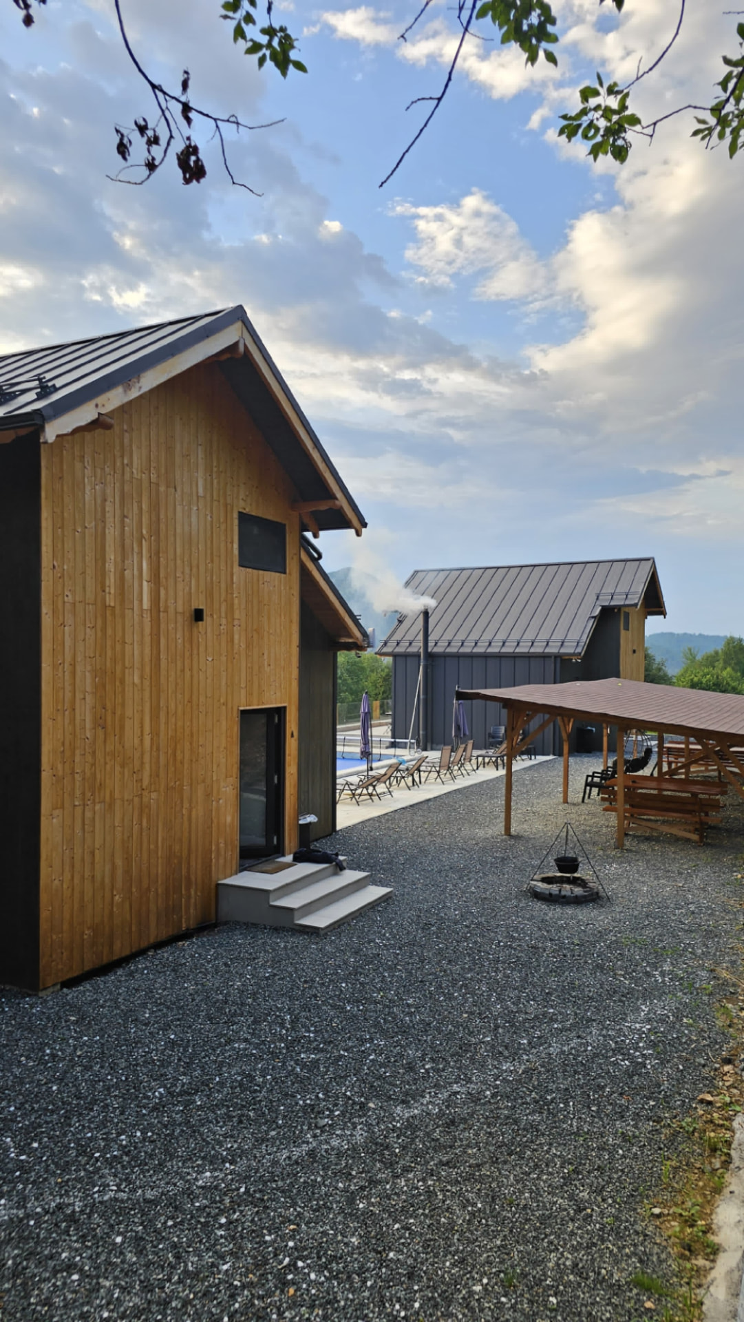 The two cabins seen from the gravel courtyard, with the wooden gazebo and fire pit