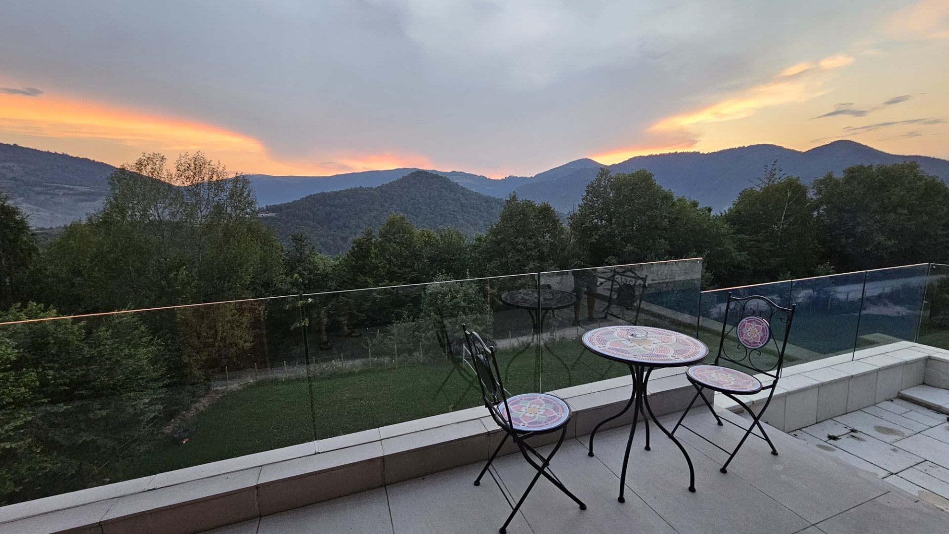 A small terrace table with two chairs, facing the mountains at sunset