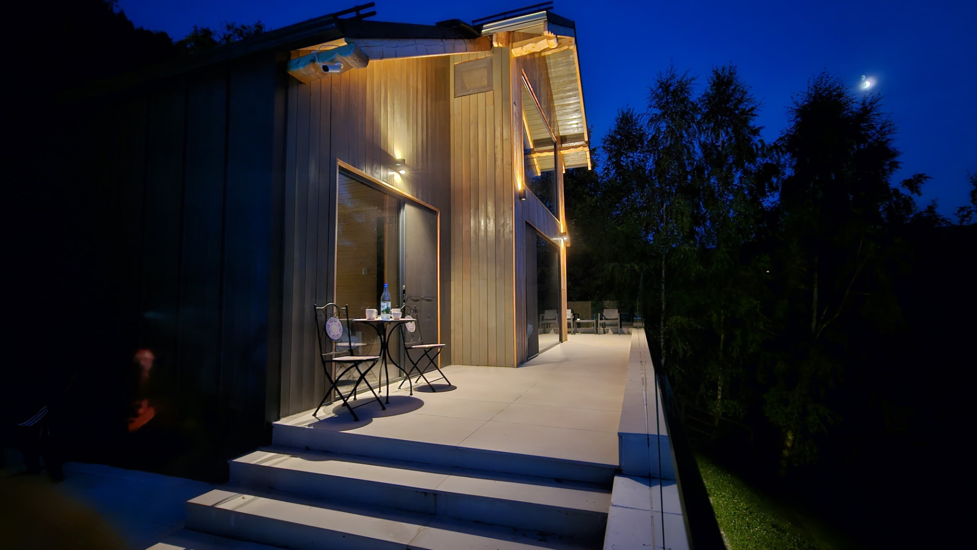 The timber façade and terrace with a small table for two, in the blue light of evening