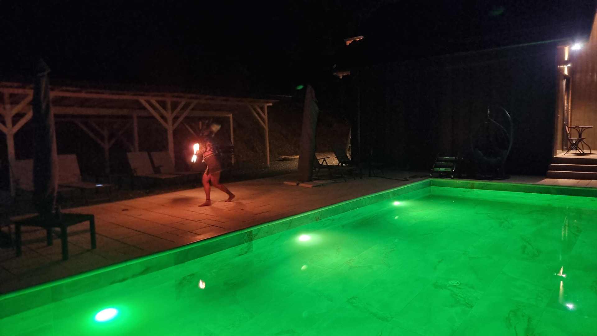 A fire show by the green-lit pool at night